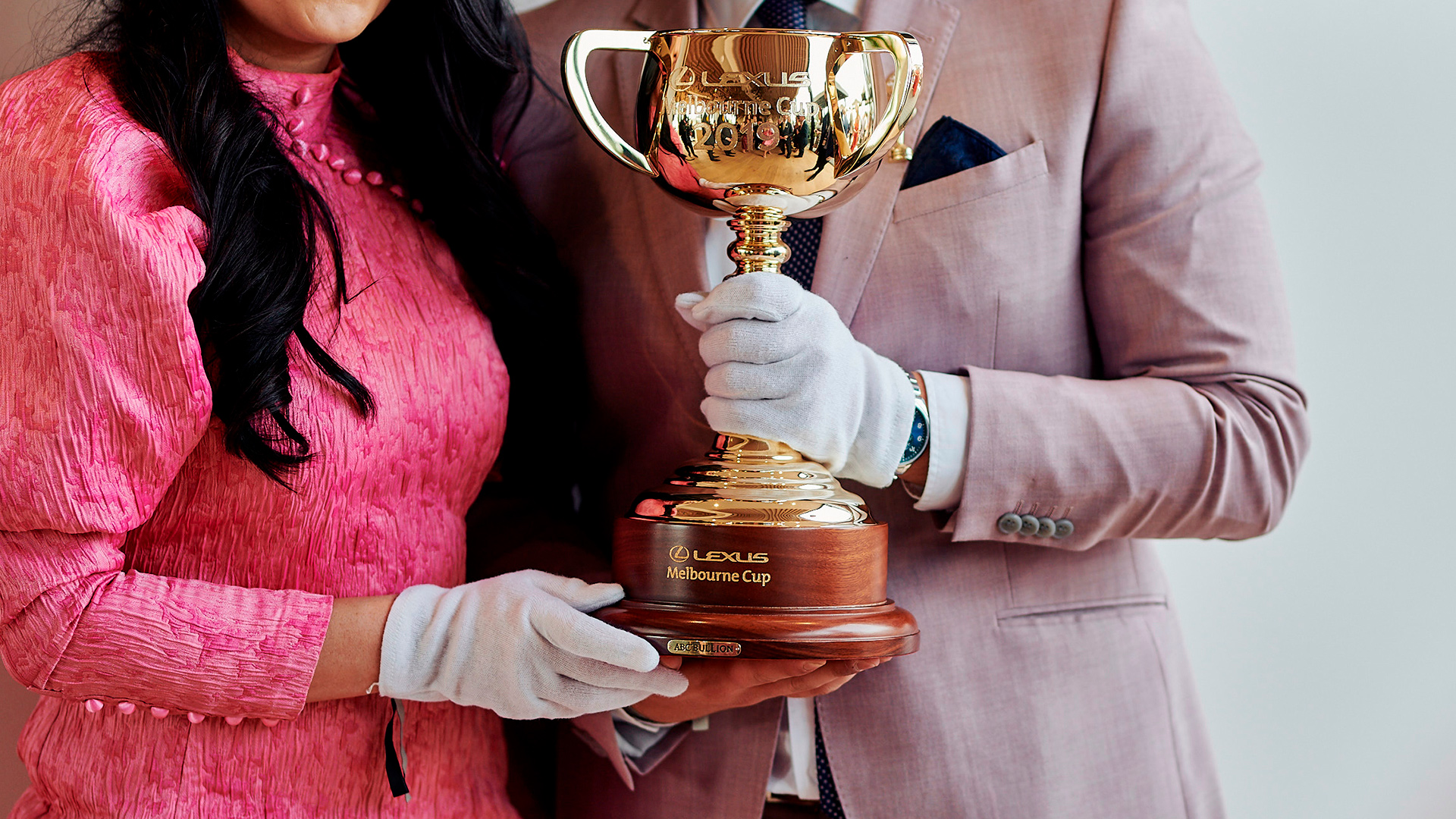 The 2019 Melbourne Cup held by a woman and man both wearing shades of pink, and white gloves.