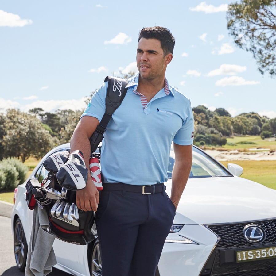 Professional golfer Dimitrios Papadatos stands beside a white Lexus, holding a golf bag on a sunlit golf course.
