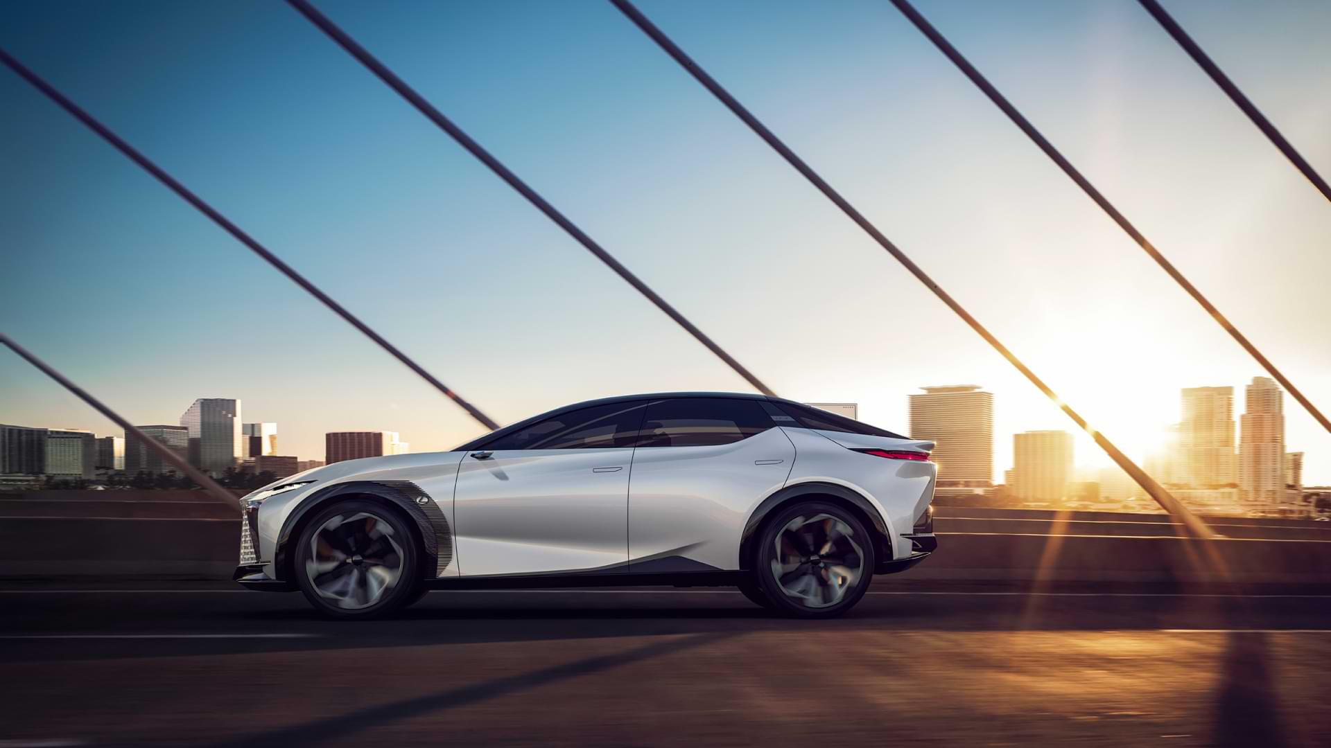 Lexus LF-Z Electrified concept vehicle driving along a bridge with the sun and a city in the background