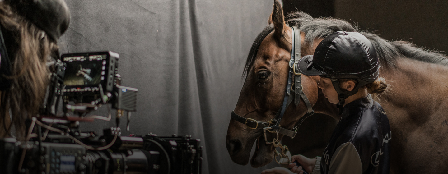 A handler stands beside a bridled horse during a behind-the-scenes film shoot.