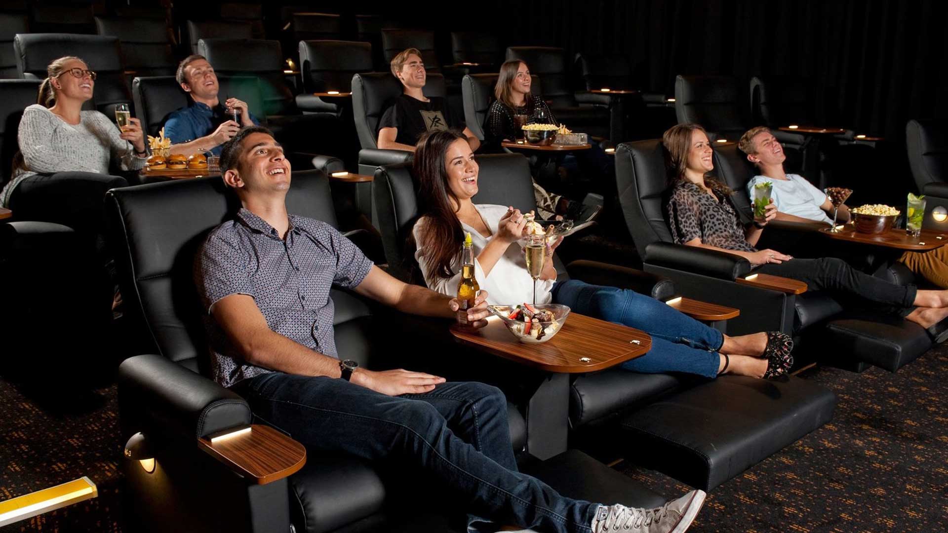 A couple relax in Gold Class cinema seats with food and drinks during a movie screening.