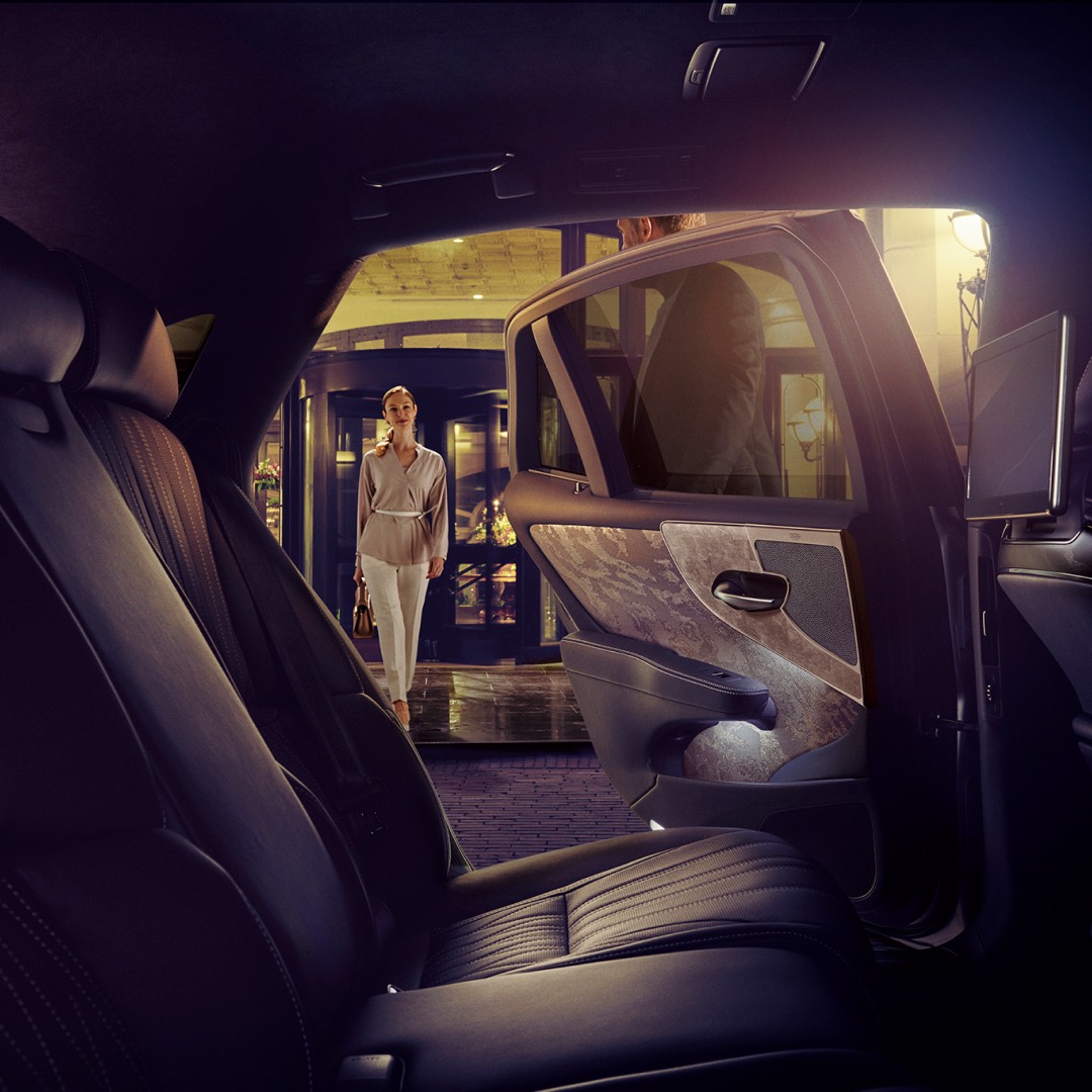 Interior rear view of a Lexus LS with woman approaching the vehicle, rear door held open by a man outside a hotel.