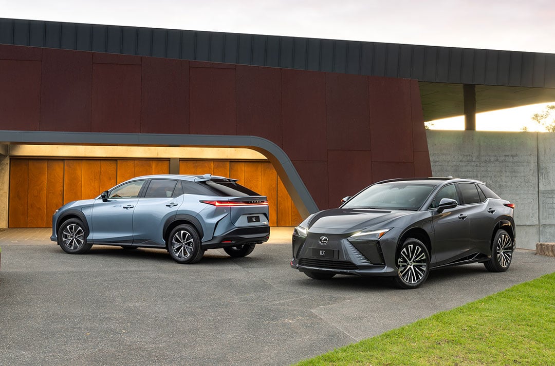 Two Lexus electrified SUVs, black and blue, parked outside a contemporary building