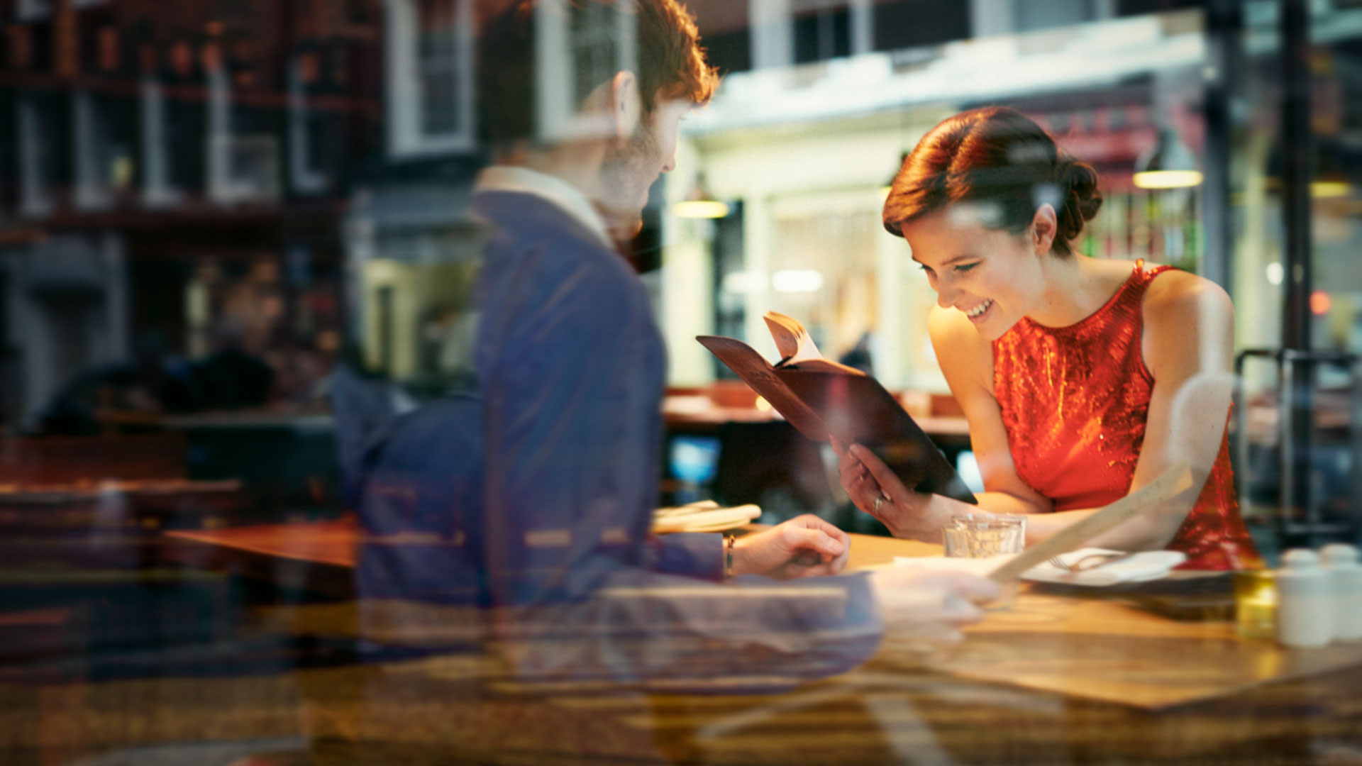 Lady in red top reading a book in a cafe opposite man in suit