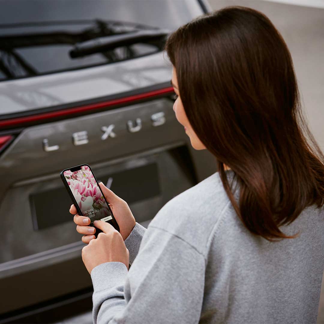 A woman looks at her phone in front of a Lexus vehicle