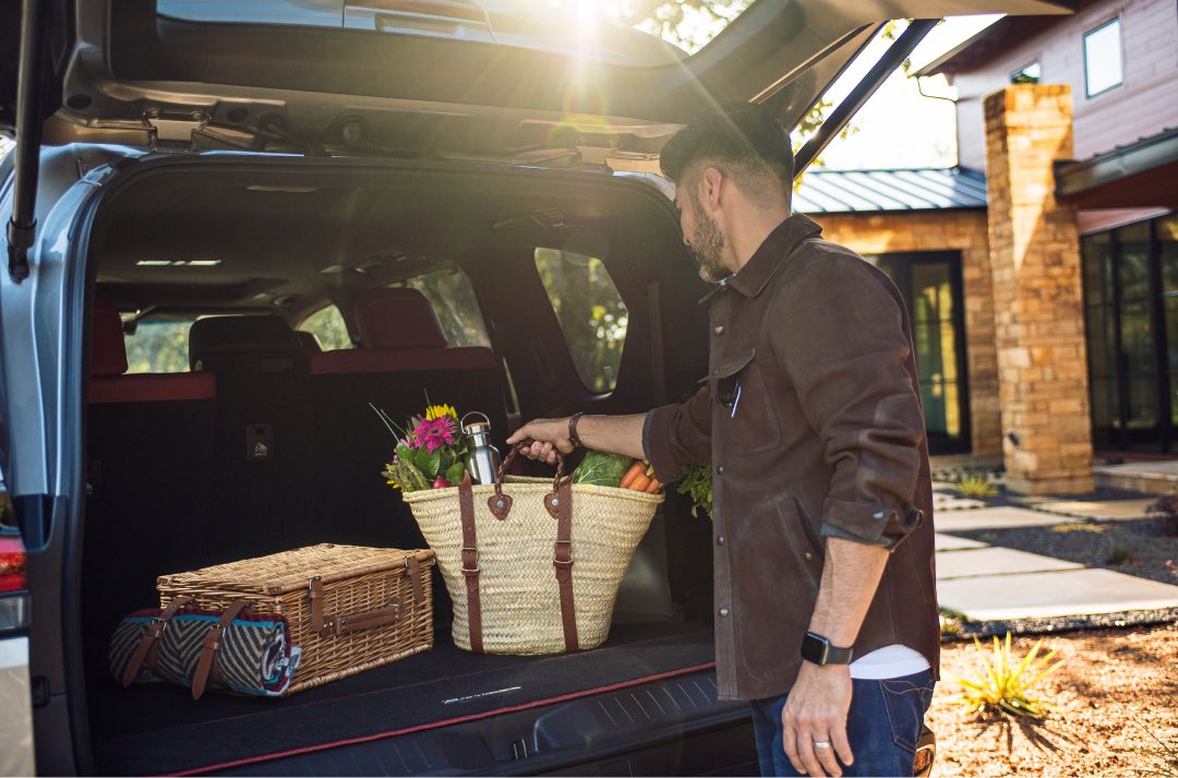 Man puts a whicker basket, filled with groceries and flowers, into the boot of a Lexus LX