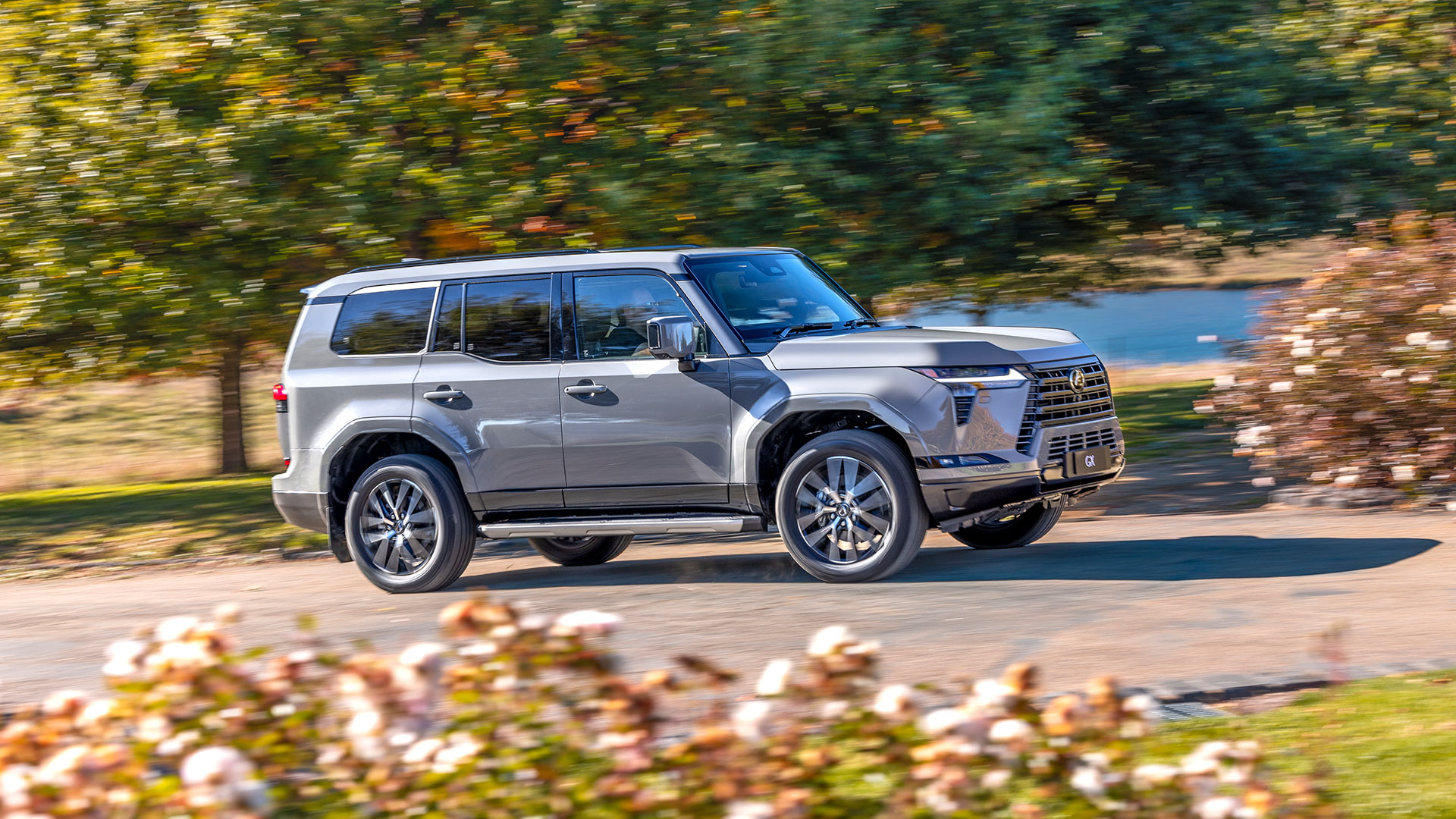 A grey Lexus GX drives along a road surrounded by trees 