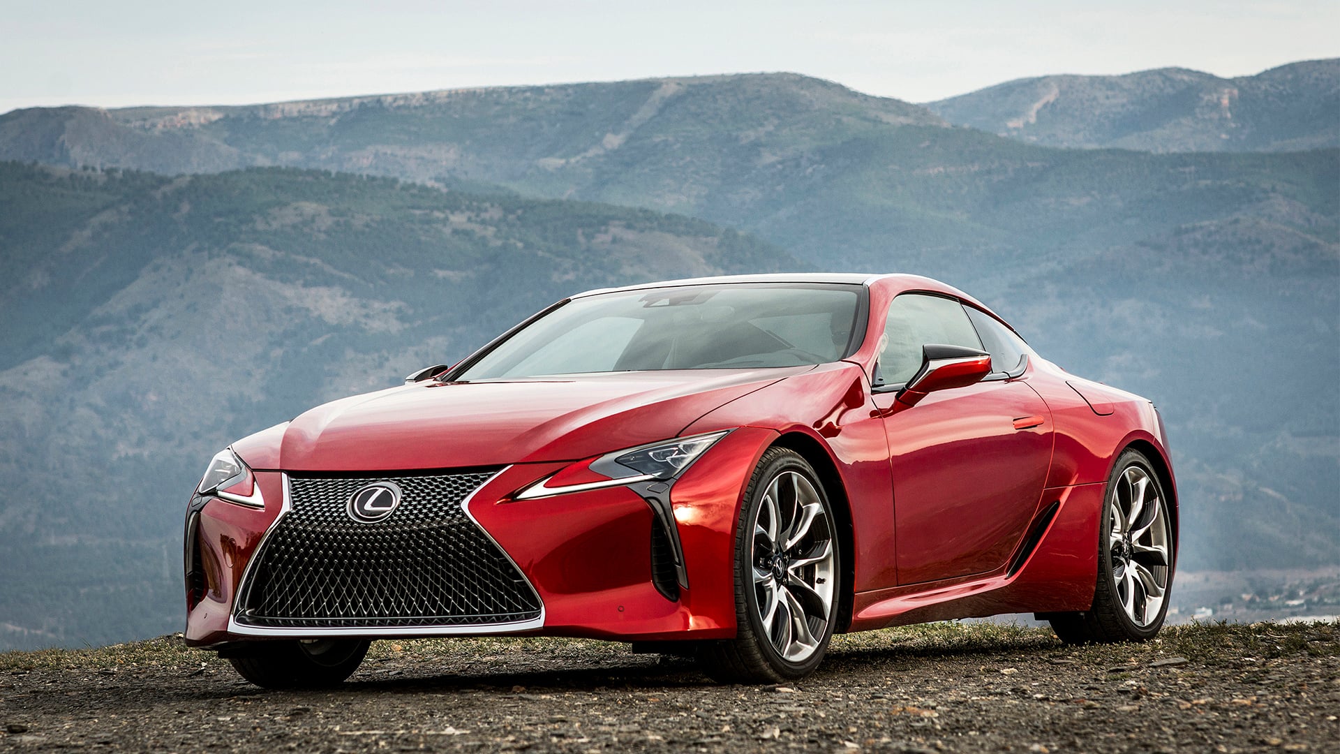 A red LC 500 coupe parked on gravel with mountains in the background