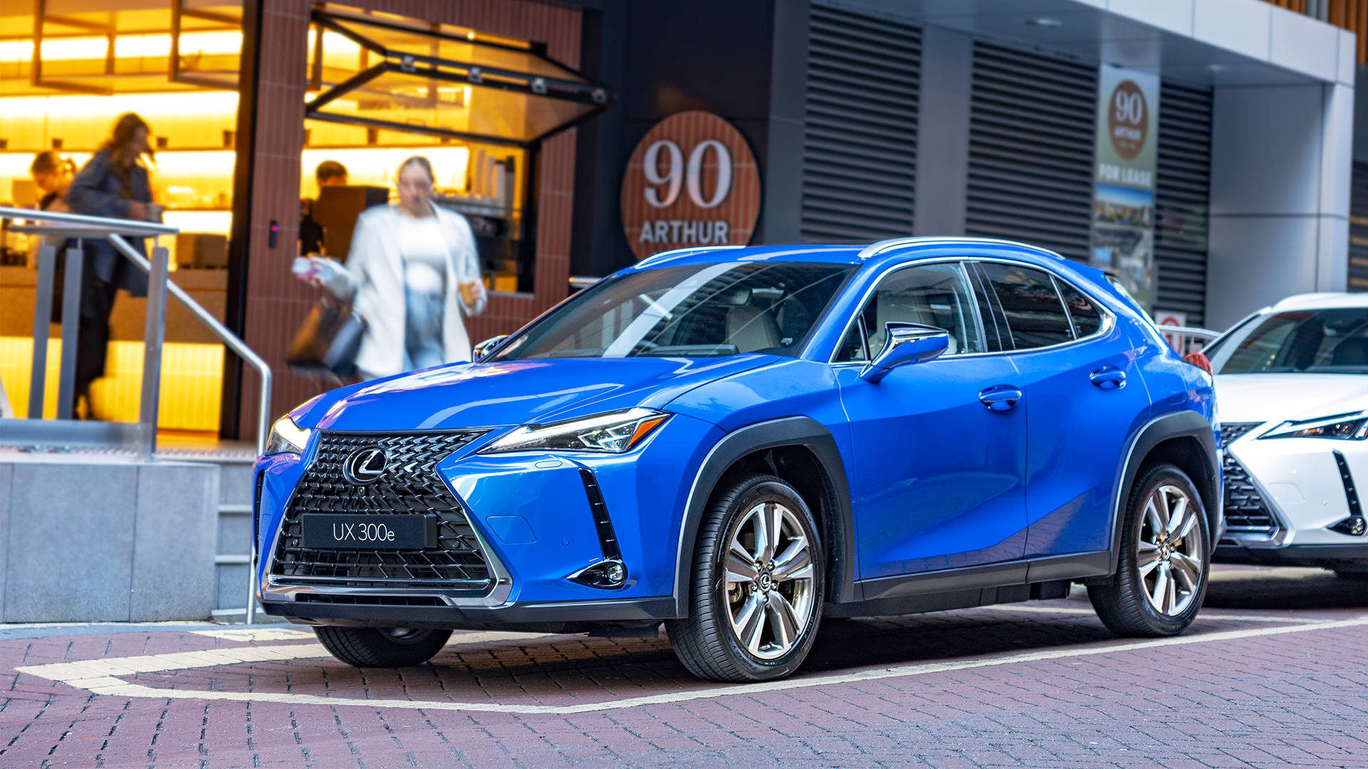A blue UX 300e parked outside a building with people behind.