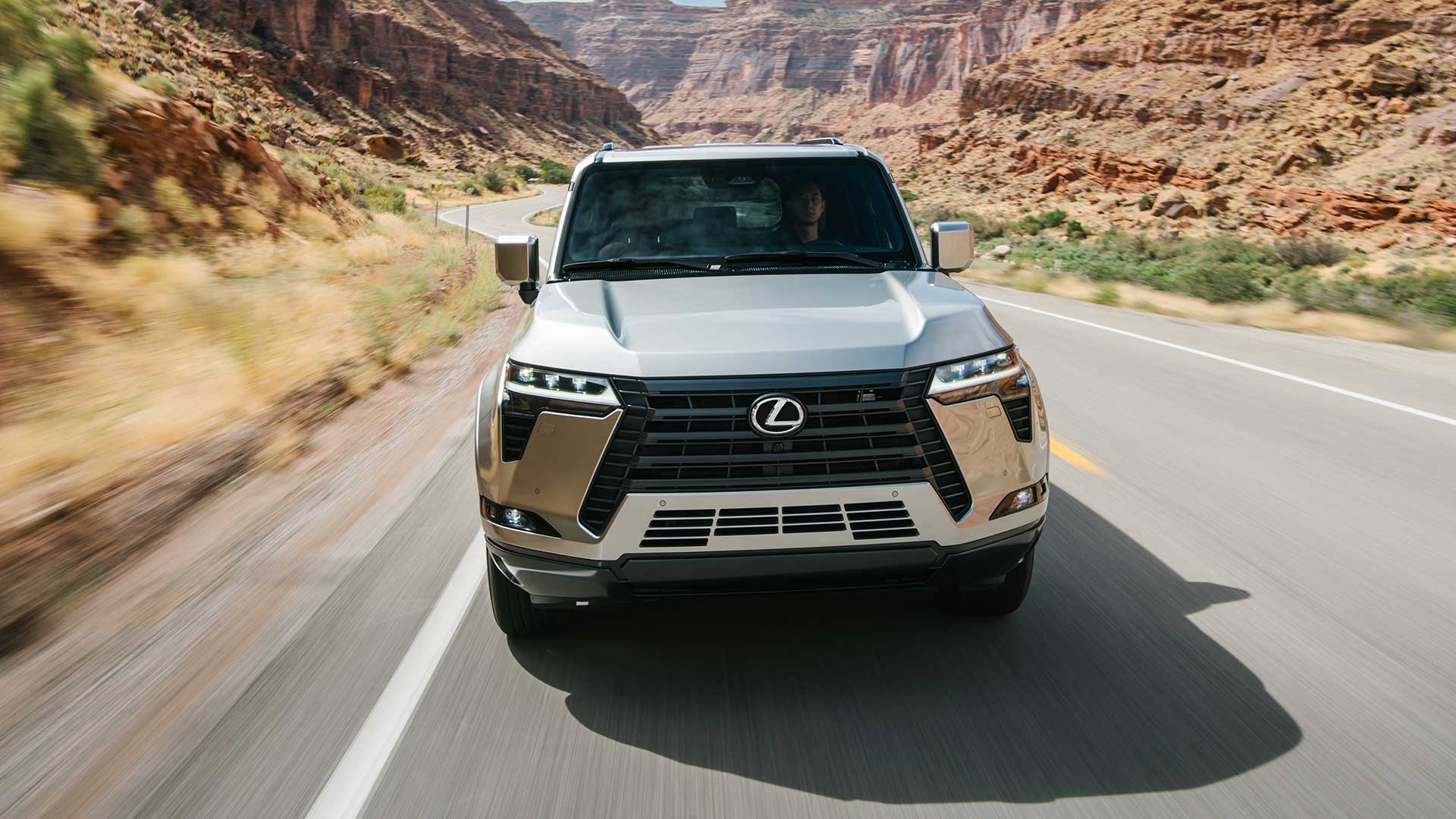 Front view of a silver 2024 Lexus GX 550 SUV driving on a canyon road. 