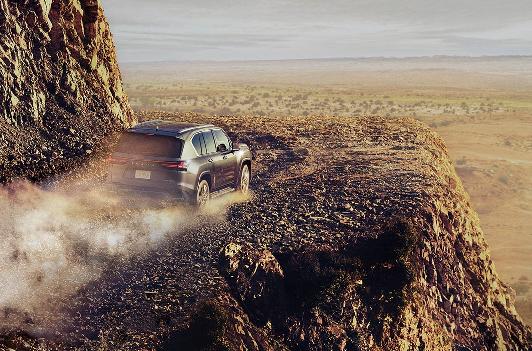 A Lexus LX drives along a rocky road with a desert in the background