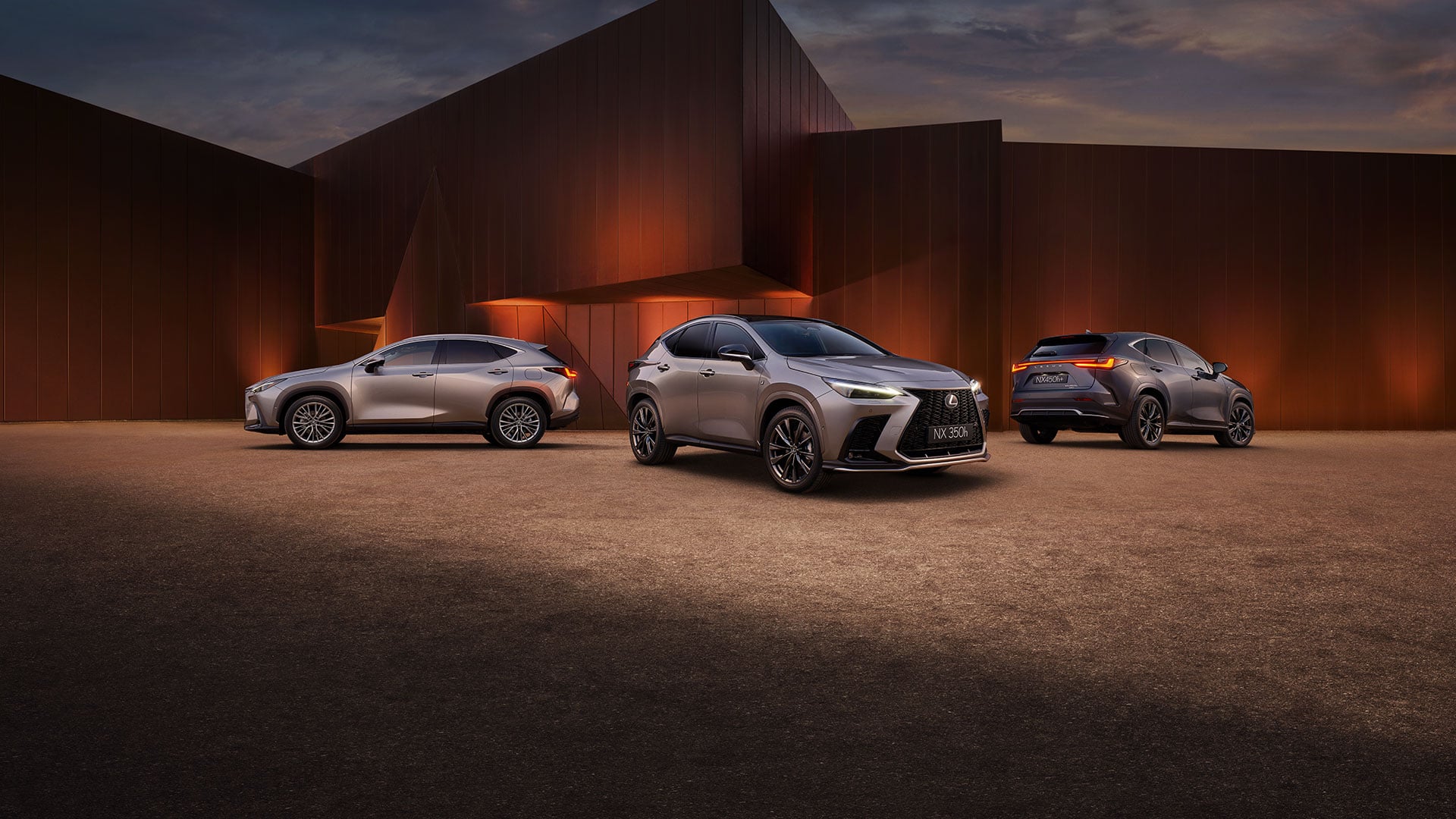 Three silver Lexus NX 350h SUVs parked at dusk in front of modern architecture.