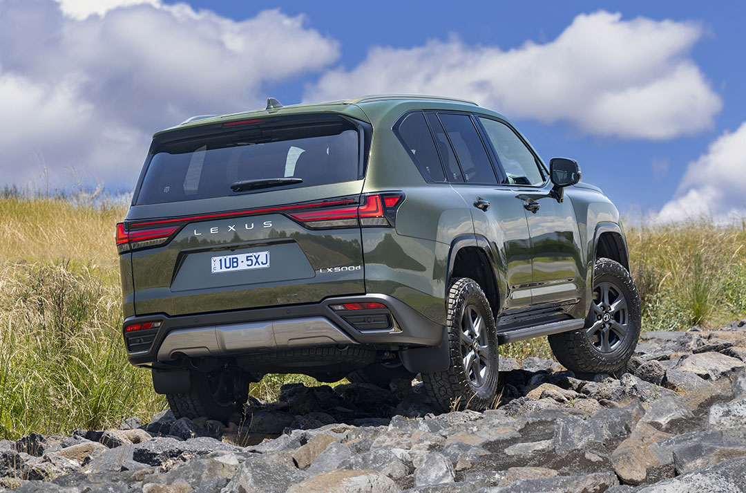 Rear view of a green Lexus LX Overtrail parked on top of rocks with a blue sky in the background