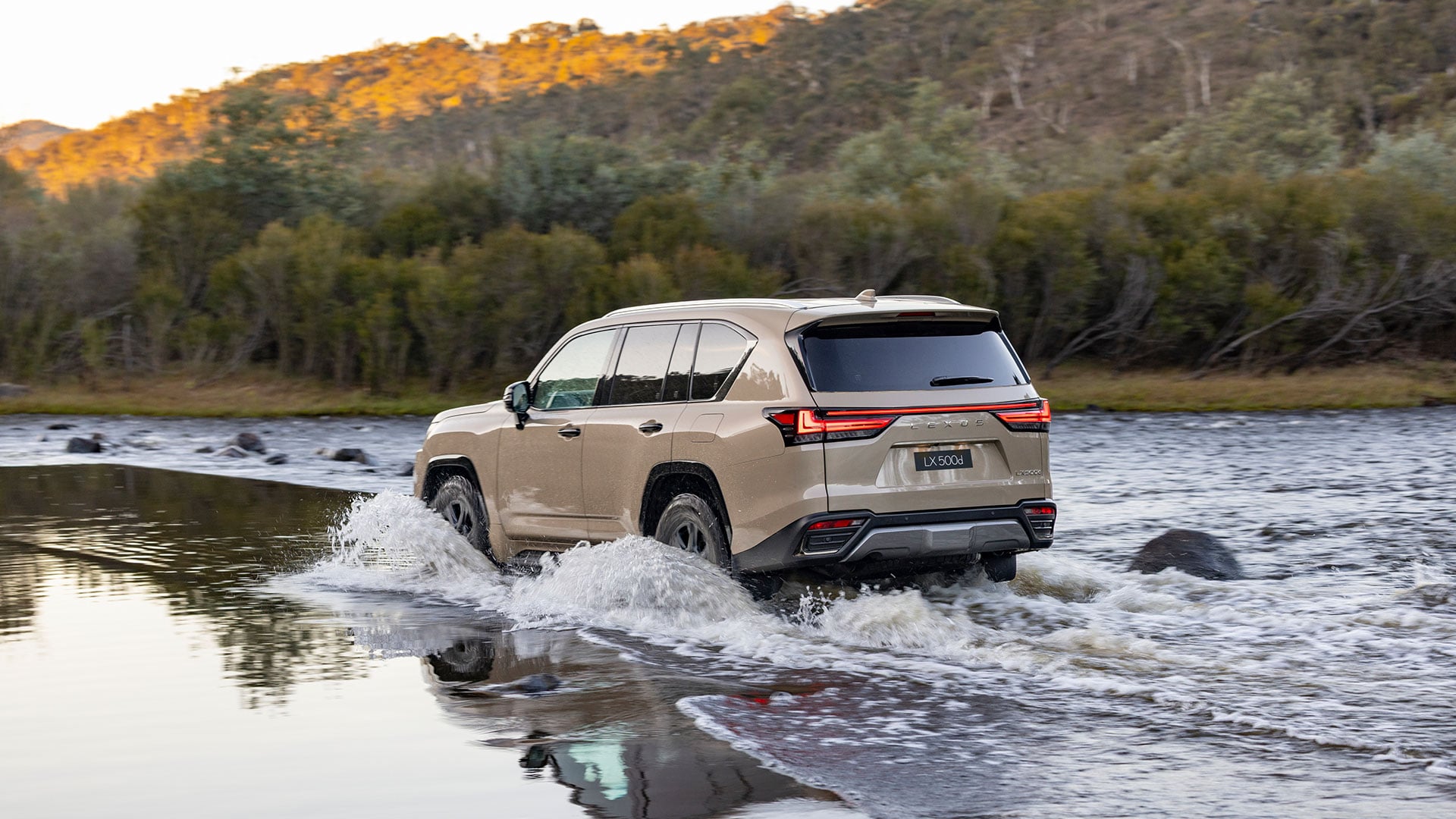 The Lexus LX 500d Overtrail in Earth tone driving across a river with water splashing
