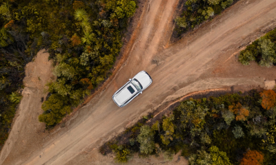 Aerial view of a white Lexus LX driving on dirt road at a crossroads surrounded by plants