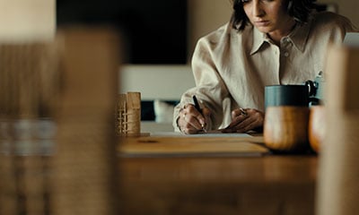 A woman writes on a wooden desk calculating finances to buy a car