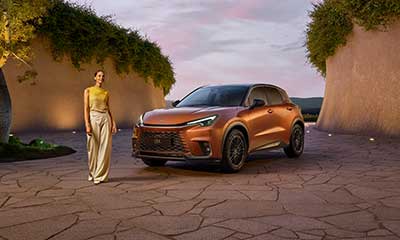 A woman stands next to an orange Lexus LBX Morizo RR concept car in an outdoor setting at dusk. 