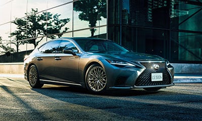 A silver Lexus LS parked on a city street next to a glass building